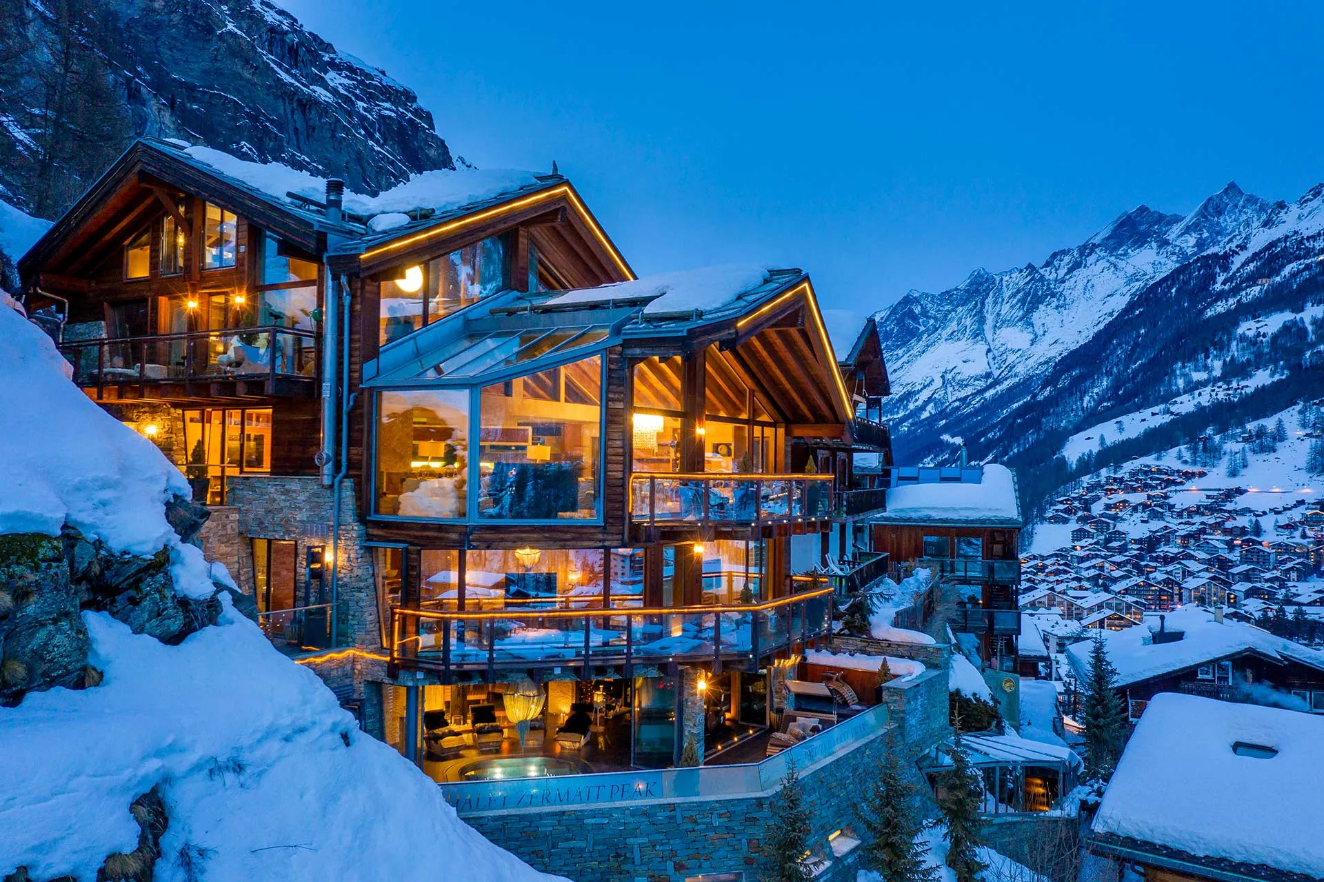 Timber chalet glowing at blue hour above a snowy alpine valley