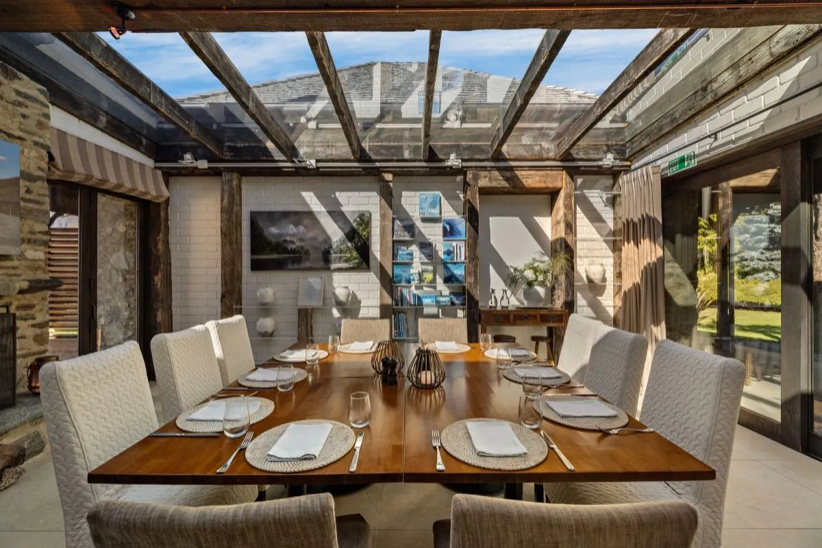 Glass-roofed dining room with stone walls and a set timber table