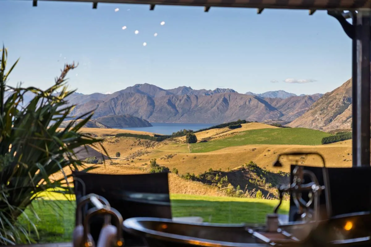 Outdoor copper bathtub on a covered terrace overlooking a lake and mountain ranges